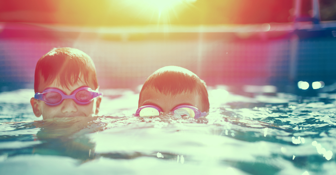 Two-little-kids-in-goggles-swimming-in-pool-at-sunset